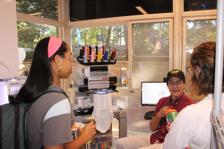 Two students talk with first-year stududent Gustavo Rios about how to use the embroidery machine.